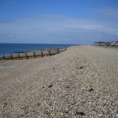 Long, slow, calm waves on a sunny day at a shallow shingle beach at Beachlands, Hayling Island